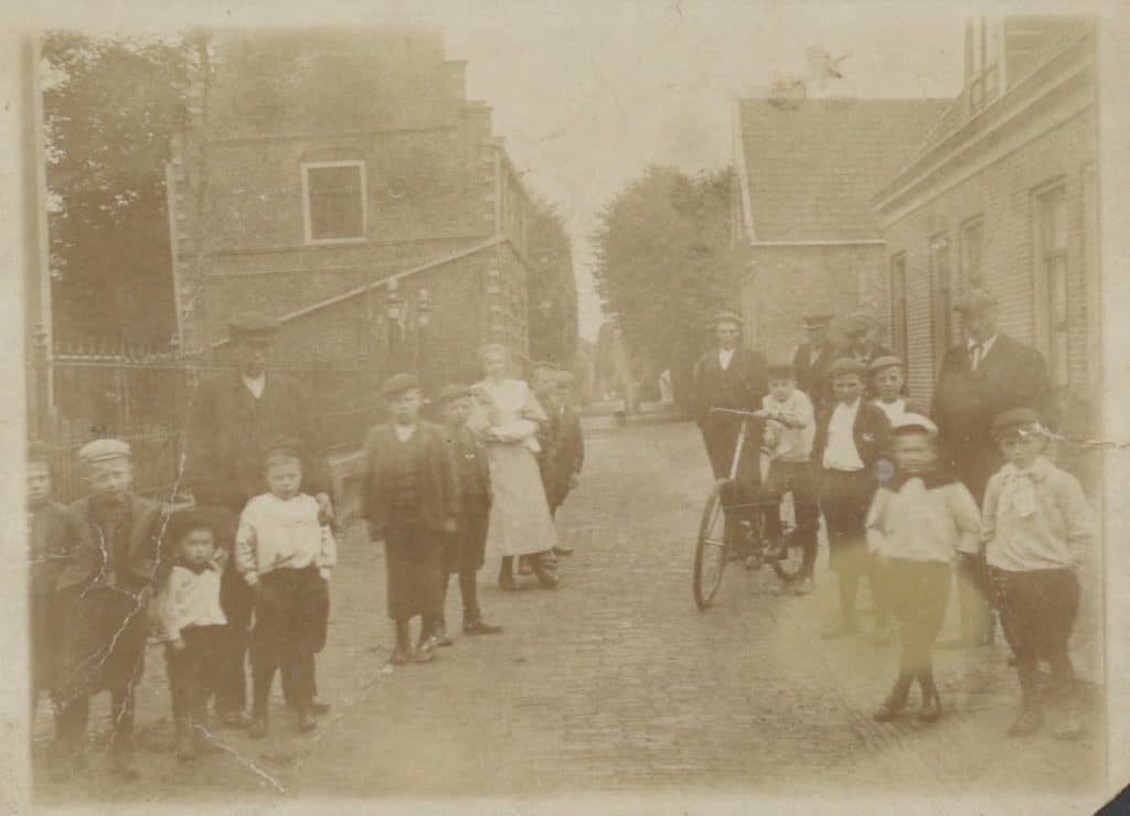 Prentbriefkaart Raadhuis Graft. Een groep Grafters staat in de Raadhuisstraat voor de kerk. Links achter hen het vervallen raadhuis: het mist onder andere zijn trapgevel aan de straatkant. Circa 1905 Collectie Kaptein.